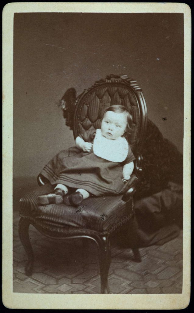 Portrett av ukjent spedbarn med mor gjemt bak stolen