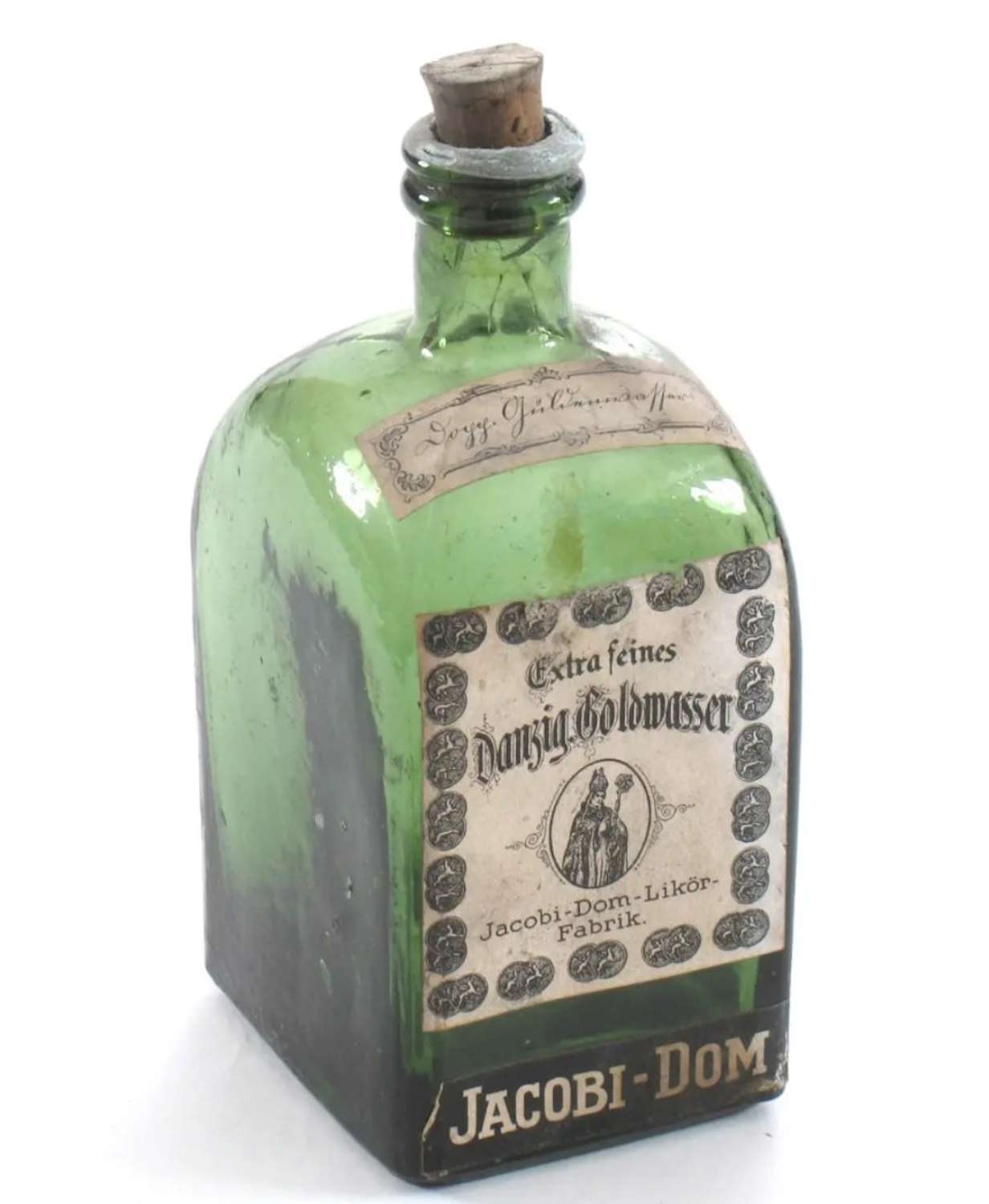 Bildet viser en grønn glassflaske med firkantet form og avrundede skuldre. Flasken har en kort hals med en kork som ser ut til å være av tre med en metallring rundt. På forsiden sitter en stor, slitt papiretikett med dekorativ ramme. Midt på etiketten står teksten «Extra feines Danzig Goldwasser», og under den er en illustrasjon av to figurer i helfigur. Nederst står teksten «Jacobi-Dom-Likör-Fabrik.» Nederst på flasken, på glasset eller en egen etikett, står teksten «JACOBI-DOM» i store bokstaver. Fargene og slitasjen gir inntrykk av en eldre gjenstand.