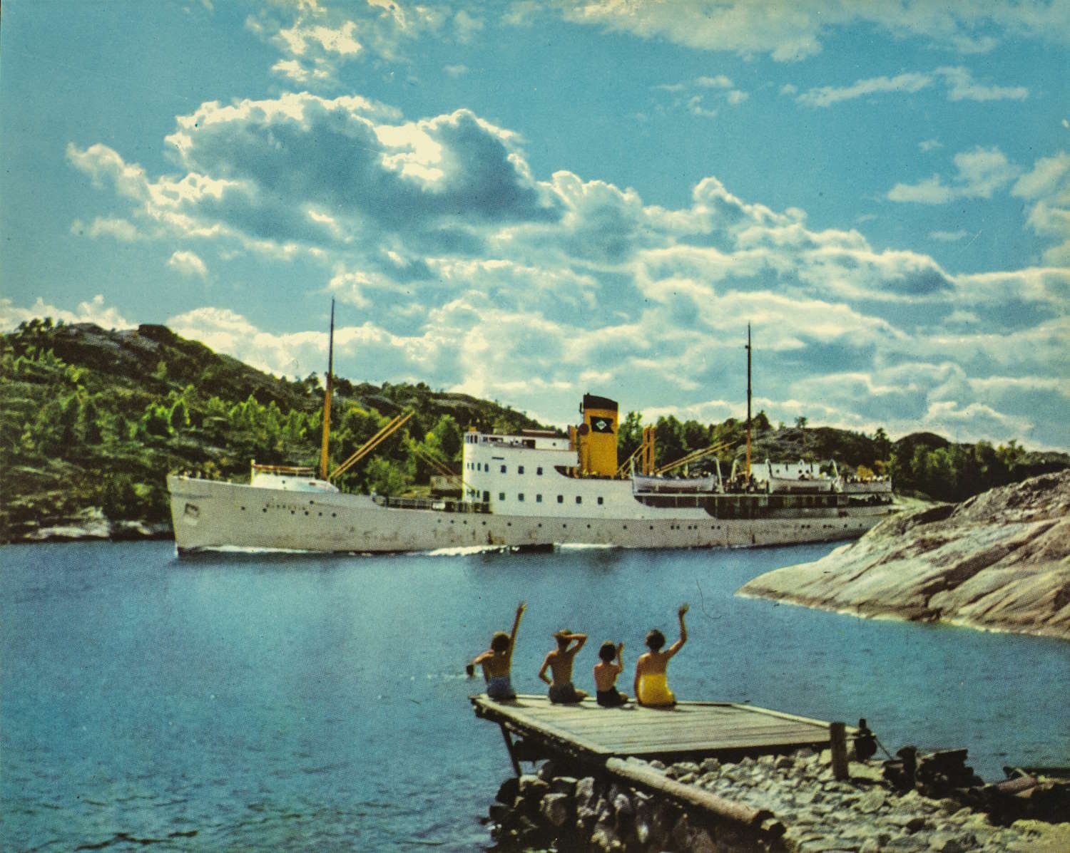Fargebilde av M/S "Bjørgvin". Et stort hvitt dampskip med to master og en gul skorstein seiler gjennom et trangt sund omgitt av skogkledde åser. Skipet er i tydelig fart, og baugen skjærer gjennom det stille blå vannet. I forgrunnen sitter fire barn på enden av en liten trebrygge. Alle vinker ivrig mot dampskipet. Til høyre i bildet ligger blankskurte svaberg som skråner ned mot sjøen. Sommerlys, lette skyer gir motivet et varmt og idyllisk preg, i kontrast til det store dampdrevne fartøyet som passerer forbi.