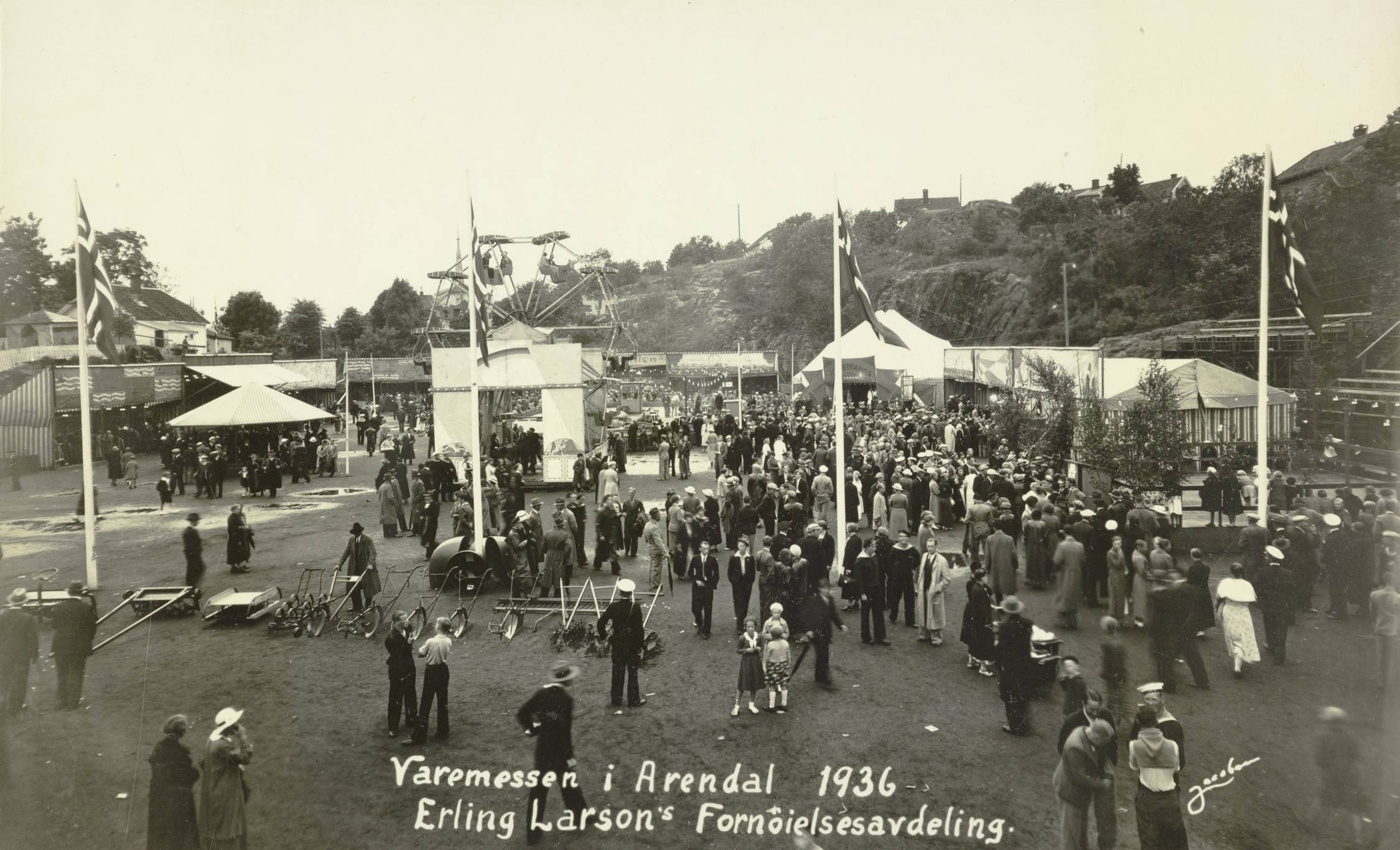 Fornøyelsesavdelingen på Idrettsplassen under varemessen i Arendal i 1936. Foto: Jacobsen. Bildet viser et stort uteområde fylt med mennesker som deltar på en fornøyelsesavdeling under en messe. I forgrunnen står små grupper av mennesker spredt rundt på en gressdekt plass. De fleste er kledd i typiske 1930-tallsklær som kåper, dresser, hatter og kjoler. På midten av bildet ligger messeområdet tett med folk. Her står flere boder, telt og attraksjoner. Et stort apparat som ligner en karusell eller en mekanisk huske med høye metallstativ reiser seg midt i bildet. Flere flaggstenger med norske flagg står rundt området. Til venstre og høyre finnes store telt og små bygninger knyttet til messen. Bak i bildet ser man en bratt skråning med trær, gjerder og noen enkle tribuner. Helt bakerst skimtes hus og bygninger i et kupert landskap. Tekst nederst på bildet sier: "Varemessen i Arendal 1936 – Erling Larson's Fornøyelsesavdeling." Stemningen virker travel og livlig, med mange som beveger seg rundt for å se på ulike attraksjoner.