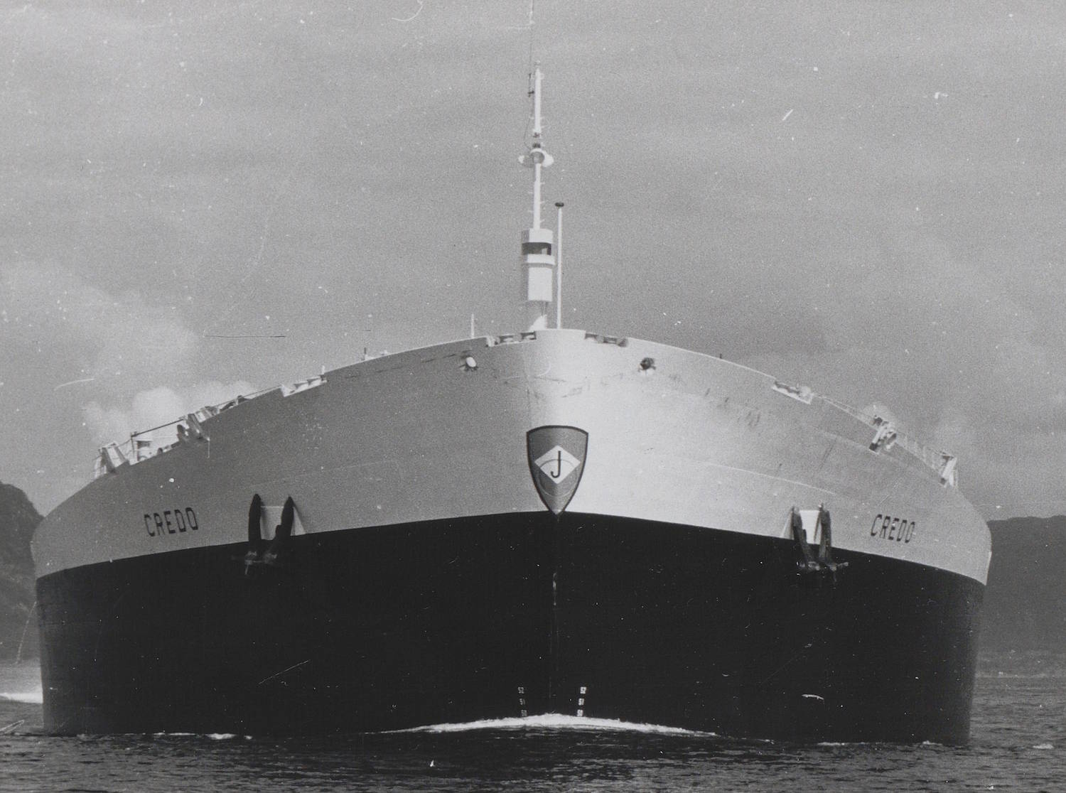 M/T "Credo" på vei til Persiagulfen 1968. Bildet er et svart-hvitt fotografi tatt ute på åpent hav. Motivet viser baugen på et svært stort skip sett rett forfra. Skipet fyller nesten hele bildeflaten og fremstår massivt og symmetrisk. Skroget er todelt i lys og mørk flate: den øvre delen er lys, mens den nedre delen er mørkere. Midt på baugen er et skjoldformet emblem synlig, og på begge sider av baugen står navnet «CREDO» malt med store bokstaver. Over baugen stiger en mast rett opp, med antenner og teknisk utstyr festet til den. Langs kanten av dekket er små detaljer som pullerter og luker synlige, jevnt fordelt på begge sider. Vannlinjen er tydelig markert, og sjøen brytes svakt mot skipets forside. Bakgrunnen består av åpent hav og en lys himmel med jevn grå tone. Ingen mennesker er synlige i bildet, og det er ingen tekst utover skipets navn og emblemet på baugen. Helhetsinntrykket er et frontalt og monumentalt portrett av et stort havgående skip under seilas.